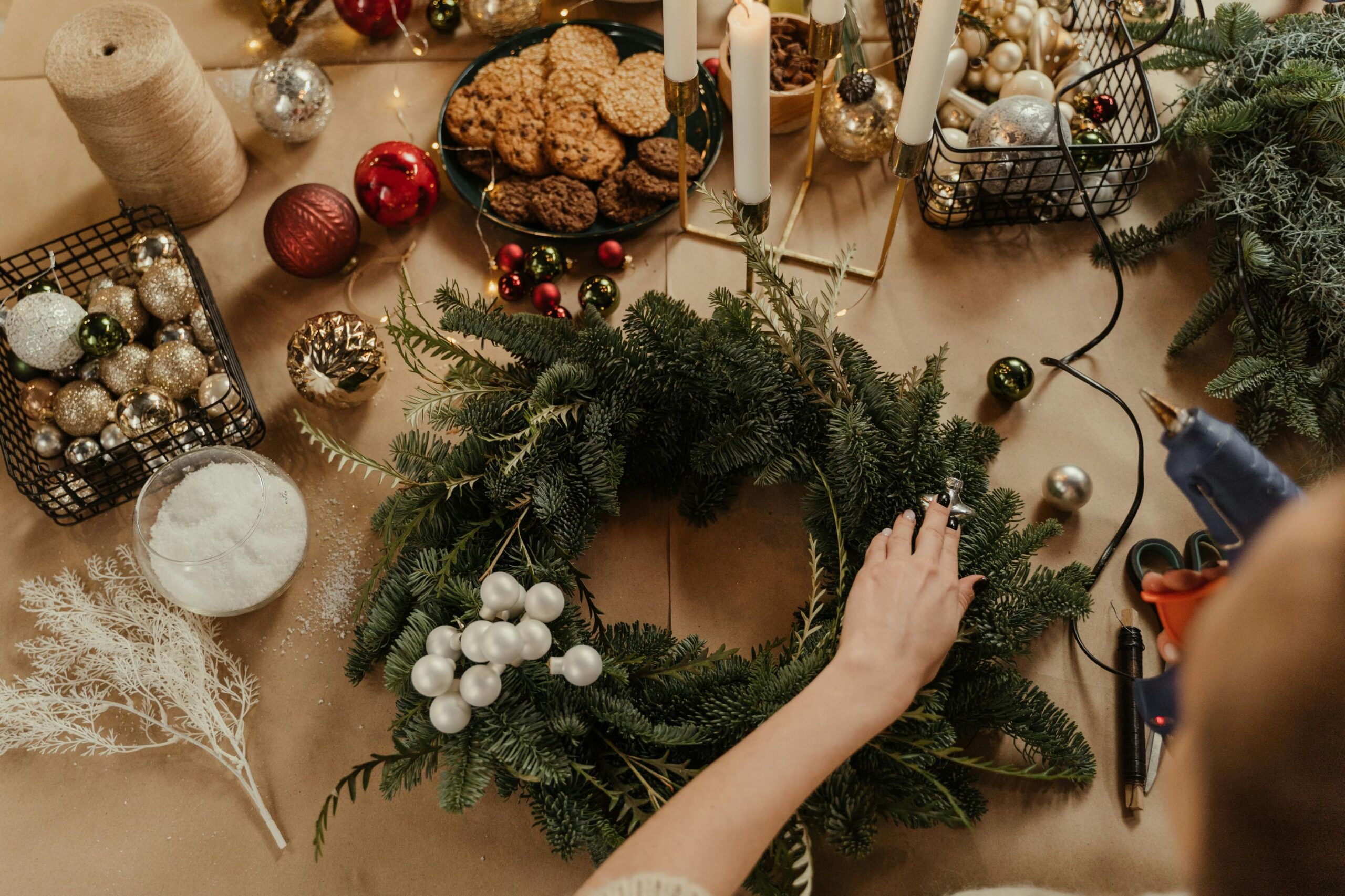 A hand glues an ornament onto a Christmas wreath